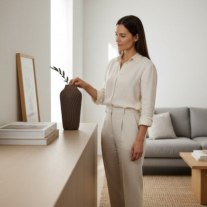 Lux Print Labs Radiate Vase, a dark brown 3D printed vase with a spiraling texture, displayed by a woman in a modern living room.